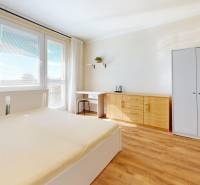 Bright bedroom in a one-room apartment with wood-patterned flooring, a wardrobe, and a bed.