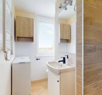 Bathroom in a studio apartment with a shower, washing machine, and floor with wooden decor.