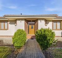A family house in Kútniky with shrubbery, a white facade, and brown accents.