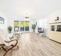 A bright living room with wood-patterned flooring, a sofa, an armchair, and a television.