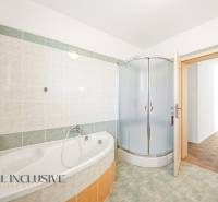 A bathroom in a family house with a bathtub, a shower corner, and tiled walls.