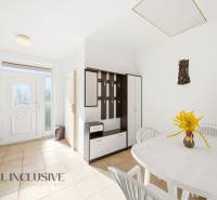The interior of a family house with a white table, plastic chairs, and a coat rack wall.