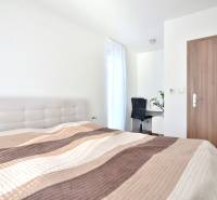 A bright bedroom with a bed, a desk, and a wooden decor floor in a three-room apartment.