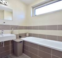A bathroom with a bathtub and a sink in a 3-room apartment with beige tiles.