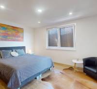 A bedroom with a comfortable armchair, a footstool, a large bed, and a floor with a wooden decor.