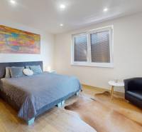 Bedroom in a family house with a bed, chair, and wooden decor flooring.