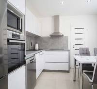 A kitchen in a 2-room apartment with glossy appliances, gray walls, and a dining table.