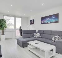 A bright living room with a corner sofa, space-themed decor, and a wood-patterned floor.