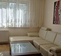 A bright living room in a three-room apartment with a sofa, an abstract painting, and a wooden decor floor.