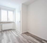 A bright room with wood-patterned flooring and a window in a three-room apartment.