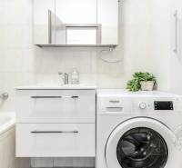 A bathroom with a bathtub, sink, and washing machine in a 2-room apartment.