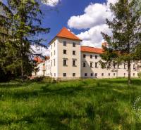 A historic building surrounded by greenery and trees on a sunny day.