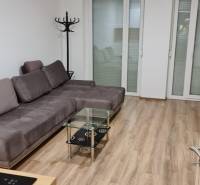 A studio apartment with a comfortable sofa, a glass table, and a floor with a wooden decor.