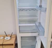 A refrigerator opening in a studio apartment with a wooden floor and a small table.
