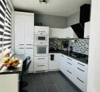 A kitchen in a 3-room apartment with white cabinets, a dark countertop, and fruit decor.