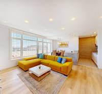A bright living space with a sofa, dining table, and wood-patterned flooring in a two-room apartment.