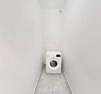 A narrow room with a washing machine in a 2-room apartment, white walls, tiled floor.
