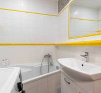 Bathroom of a holiday apartment with a bathtub, sink, washing machine, and white tiles.