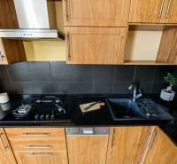 A kitchen unit in a 2-room apartment, with a wooden decor floor and dark tiles.