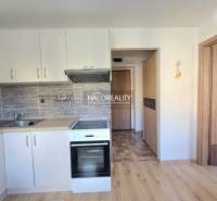 A kitchen unit with white cabinets and a wooden decor floor in a studio apartment.