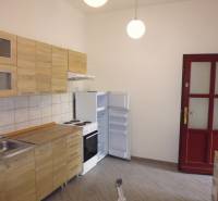 A kitchen with wooden cabinets, a wooden-patterned floor, and white appliances in a 3-room apartment.