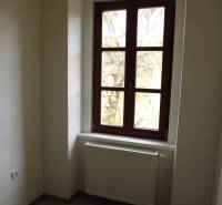 A room with a large window, a radiator, and a floor with a wooden decor in a 3-room apartment.
