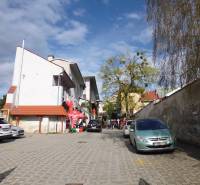In Prešov on Hlavná Street, there are parked cars and pedestrians on the paved area.