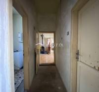 A narrow hallway leads to a room with a wooden decor floor in a family house.