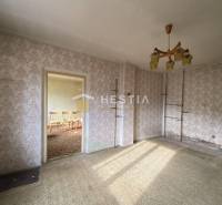 A room in a family house with floral wallpaper, carpeted floor, and a chandelier.