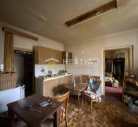A kitchen in a family house with wooden furniture, an old television, a dining table, and a wardrobe.