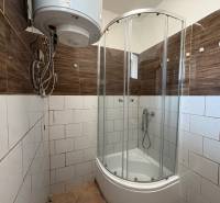 A bathroom in a family house with a corner shower, electric boiler, and brown tiles.