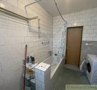 A bathroom in a family house with a bathtub, a washing machine, and tiled walls.