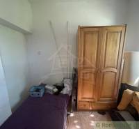 A room in a family house with a bed, a wooden wardrobe, and a window.