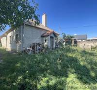 A family house in Jatov with a grassy yard and a pile of wood next to the house.