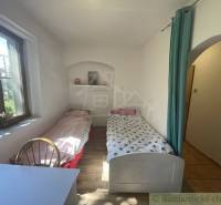 A room in a family house with two beds, a wooden-patterned floor, and a window.