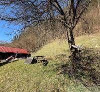 A cottage near Moštenica surrounded by trees and grassy hills under sunny weather.