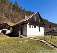 A cottage in Moštenica, surrounded by nature and forest, with a clear sky and grassy land.
