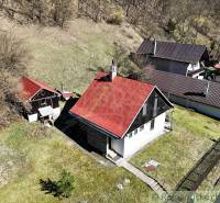 A cottage in Moštenica with a slanted red roof, surrounded by greenery and hilly terrain.