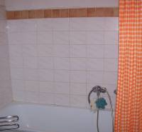 Bathroom with a bathtub, orange curtain, and tiles in a 2-room apartment.