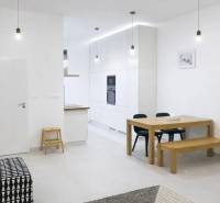 Interior of a 2-room apartment with white walls, a wooden table, and a black sofa.