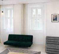 Living room with white walls, a green sofa, a patterned armchair, and curtains.