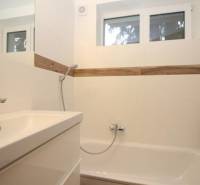 Bathroom with a bathtub and a sink in a studio apartment, white tiles, wooden decor.