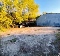 Commercial land in Nitra with a metal hall and fencing in a wooded environment.