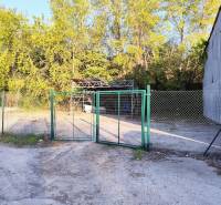 A fence with a gate and a metal structure surrounded by trees in the commercial area of Nitra.
