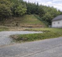 A sloped plot of land in the village of Makov with an access road and surrounding forest vegetation. Land - residential.