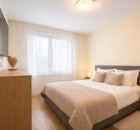 A bedroom in a 3-room apartment with a gray bed, a floor with a wood decor, and a TV on the wall.