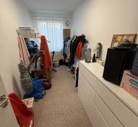 A narrow room in a 4-room apartment with a chest of drawers, shelves, and a window without curtains.