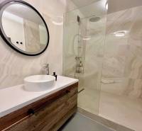 Bathroom with a wooden cabinet, round mirror, and shower in a 3-room apartment.