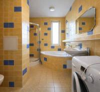 A bathroom in a 3-room apartment with a bathtub, shower, and washing machine, tiled with yellow tiles.