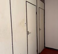White doors in a 2-room apartment with a dark floor and a wall lamp.